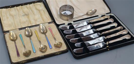 A cased set of six George V enamelled silver coffee spoons, a set of six silver handled tea knives, a napkin ring